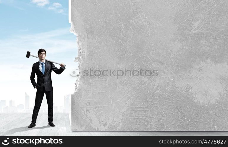 Overcoming challenges. Young determined businessman with hammer in hands