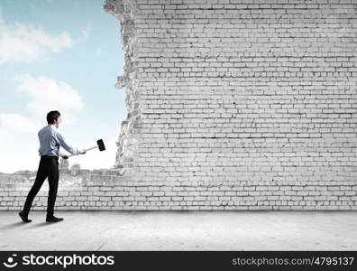 Overcoming challenges. Young determined businessman with hammer in hands