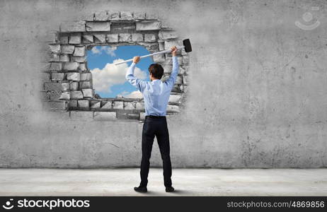 Overcoming challenges. Young determined businessman with hammer in hands