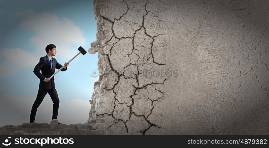 Overcoming challenges. Young determined businessman with hammer in hands