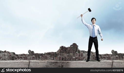 Overcoming challenges. Young determined businessman with hammer in hands