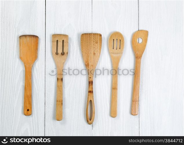Overhead angled shot of wooden spatula, spoons on white wood. Format in horizontal layout.
