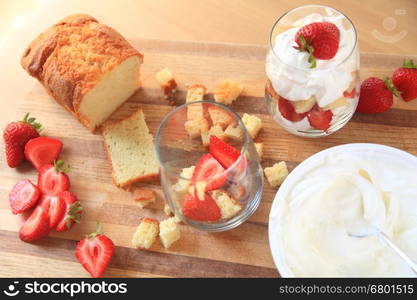 Overhead of strawberries, whipped cream and pound cake with finished miniature trifle on cutting board