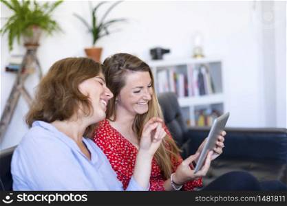 Overhead photograph of two beautiful young women at home sitting on sofa while using a tablet PC computer and smiling