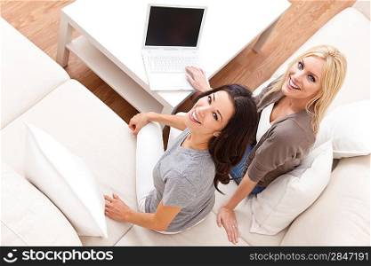 Overhead photograph of two beautiful young women at home sitting on sofa or settee using a laptop computer and smiling