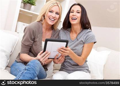 Overhead photograph of two beautiful young women at home sitting on sofa or settee using a tablet PC computer and smiling