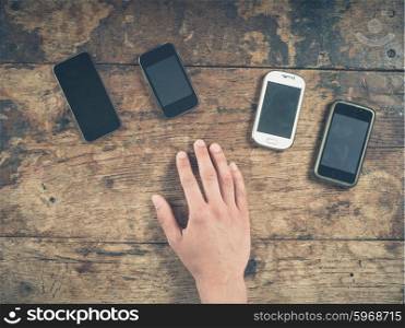 Overhead shot of a male hand resting on a wooden table with a selection of smart phones