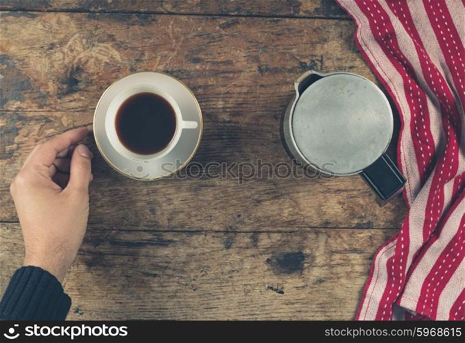 Overhead shot of a male hand with a cup of coffee, a tea towel and a moka pot on a wooden table