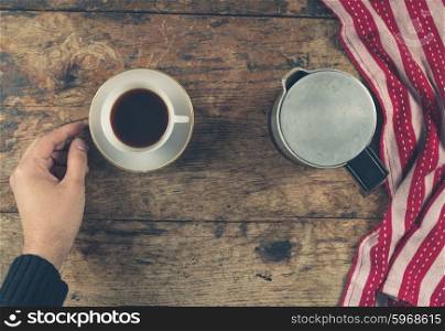 Overhead shot of a male hand with a cup of coffee, a tea towel and a moka pot on a wooden table