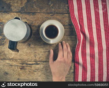 Overhead shot of a male hand with a cup of coffee and a tea towel on a wooden table