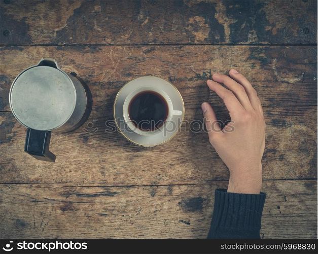 Overhead shot of a male hand with a cup of coffee on a wooden table