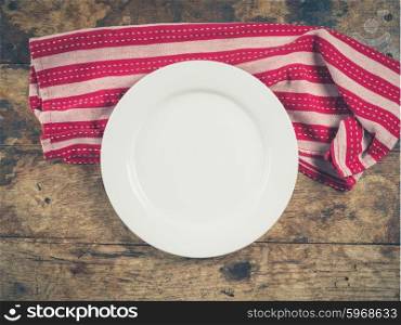 Overhead shot of a white plate and a tea towel on a wooden table