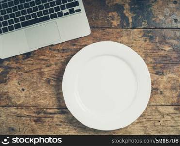 Overhead shot of a white plate and laptop on a wooden table