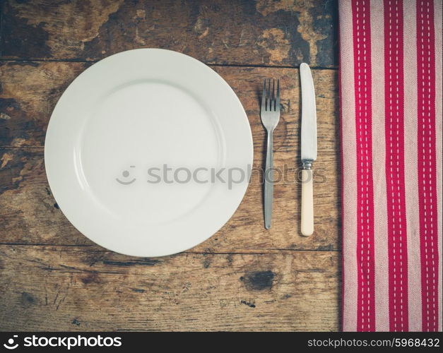 Overhead shot of a white plate with a knife and fork on a wooden table with a tea towel