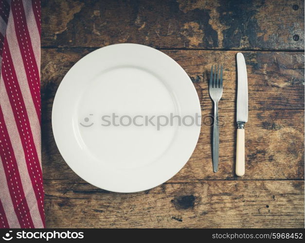 Overhead shot of a white plate with a knife and fork on a wooden table with a tea towel