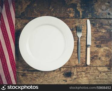 Overhead shot of a white plate with a knife and fork on a wooden table with a tea towel