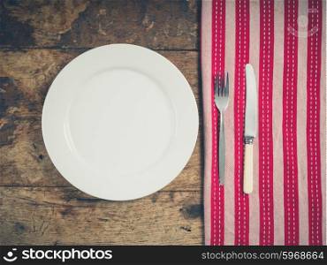 Overhead shot of a white plate with a knife and fork on a wooden table with a tea towel