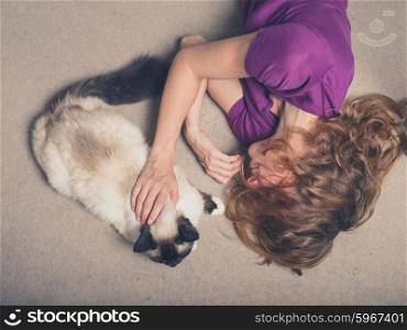 Overhead shot of a young woman lying on a carpet at home and petting a cat