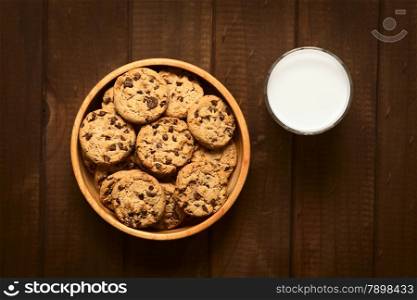 Overhead shot of chocolate chip cookies in wooden bowl with a glass of cold milk on the side photographed on wood with natural light. Chocolate Chip Cookies with Milk