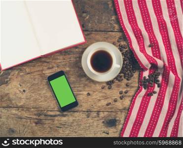 Overhead shot of coffee concept with cup, tea towel, an open book and a smart phone with a green screen