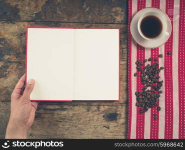 Overhead shot of coffee concept with cup, tea towel and a person holding a book