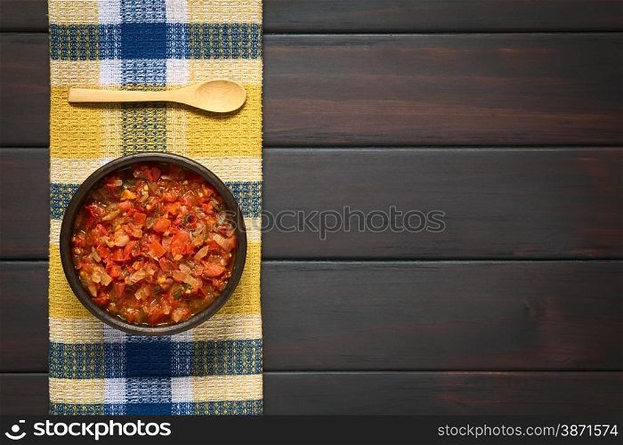 Overhead shot of Colombian hogao or criollo sauce (salsa criolla) made of cooked onion and tomato, served as accompaniment to traditional dishes. Photographed on dark wood with natural light.