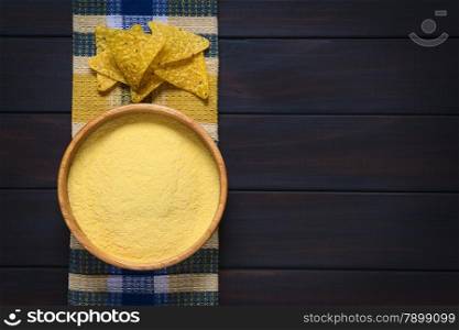 Overhead shot of cornmeal in wooden bowl with tortilla chips on kitchen towel, photographed on dark wood with natural light