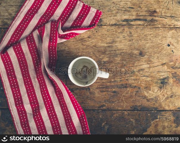 Overhead shot of empty cup and red and white tea towel on a wooden surface