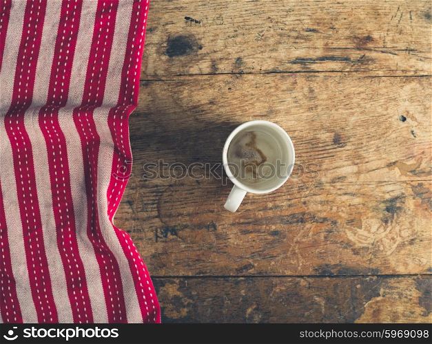 Overhead shot of empty cup and red and white tea towel on a wooden surface