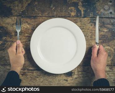 Overhead shot of hands holding a knife and fork by a white plate on a wooden table