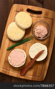 Overhead shot of liverwurst spread on bun with chives, knife and buns on wooden board, photographed with natural light