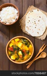 Overhead shot of pumpkin, mangold, potato and tomato curry dish in wooden bowl with homemade chapati flatbread and rice photographed with natural light
