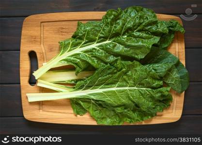 Overhead shot of raw chard leaves (lat. Beta vulgaris) on wooden board, photographed on dark wood with natural light