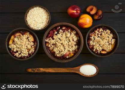 Overhead shot of three rustic bowls filled with baked plum and nectarine crumble or crisp, photographed on dark wood with natural light