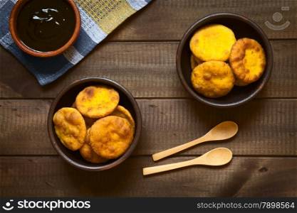 Overhead shot of traditional Chilean Sopaipilla fried pastry made with mashed pumpkin in the dough, served with Chancaca sweet sauce, photographed on dark wood with natural light