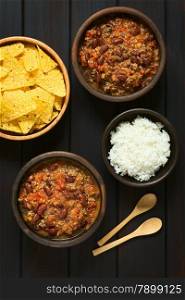 Overhead shot of two bowls of chili con carne with rice and tortilla chips, photographed on dark wood with natural light