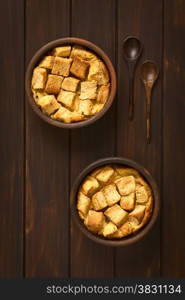 Overhead shot of two rustic bowls of bread pudding made of diced stale bread, milk, egg, cinnamon, sugar and butter, photographed on dark wood with natural light