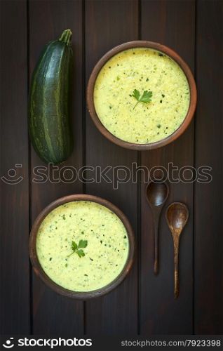 Overhead shot of two rustic bowls of cream of zucchini soup garnished with parsley leaf, photographed on dark wood with natural light