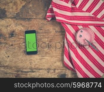 Overhead shot of yogurt and smart phone with a green screen on a wooden table with a tea towel