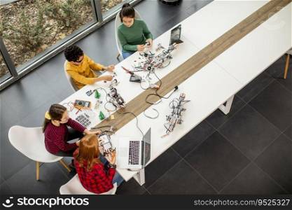Overhead view at group of happy kids programming electric toys and robots at robotics classroom