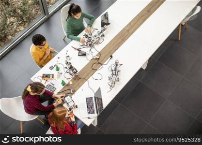 Overhead view at group of happy kids programming electric toys and robots at robotics classroom