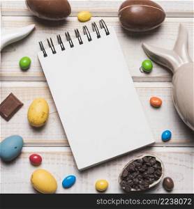 overhead view blank spiral notepad with easter eggs candies choco chips wooden desk