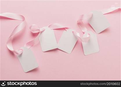 overhead view blank tags pink ribbon against plain pink backdrop