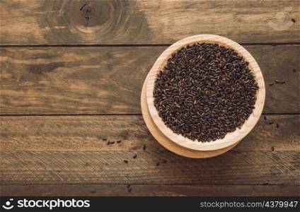 overhead view bowl with black rice grain wooden background