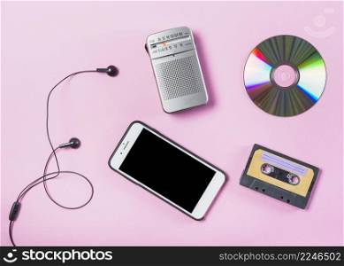 overhead view cellphone with earphone cd radio cassette pink background