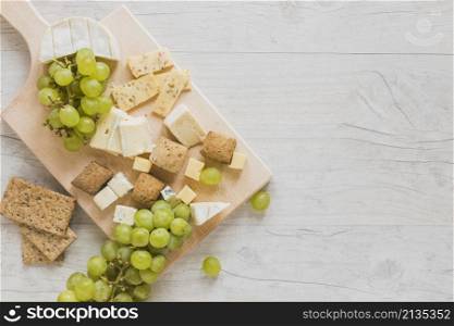 overhead view cheese blocks crisp bread grapes wooden desk