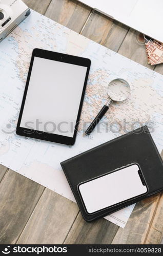 overhead view digital tablet cell phone magnifying glass diary map against wooden backdrop