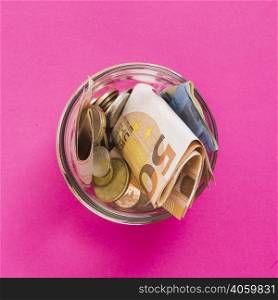overhead view euro banknotes coins open glass jar against pink background