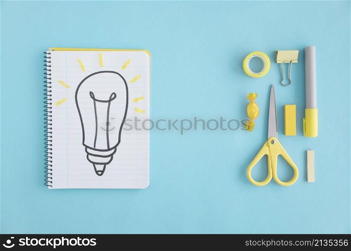 overhead view hand drawn light bulb notebook with stationary blue background