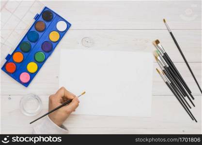 overhead view human hand painting white blank paper with paint brush